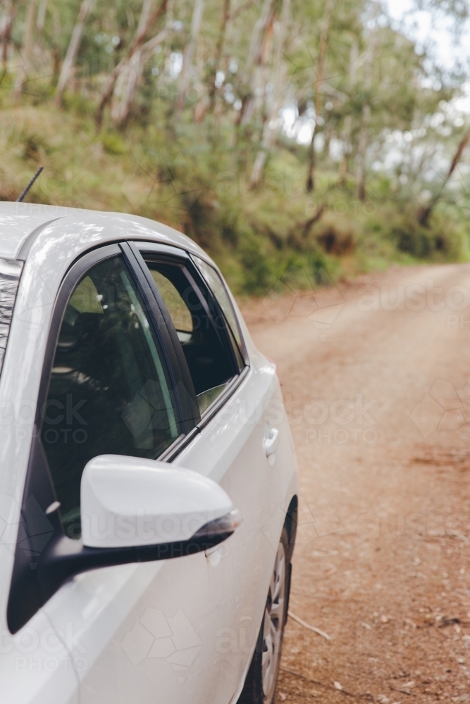 White car on unsealed road trip in green countryside with window open - Australian Stock Image