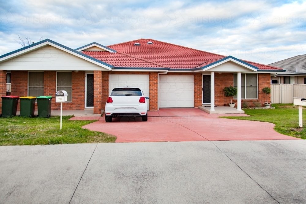 White car parked outside residential suburban brick house - Australian Stock Image