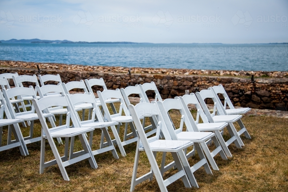 White chairs set up beside ocean for wedding - Australian Stock Image
