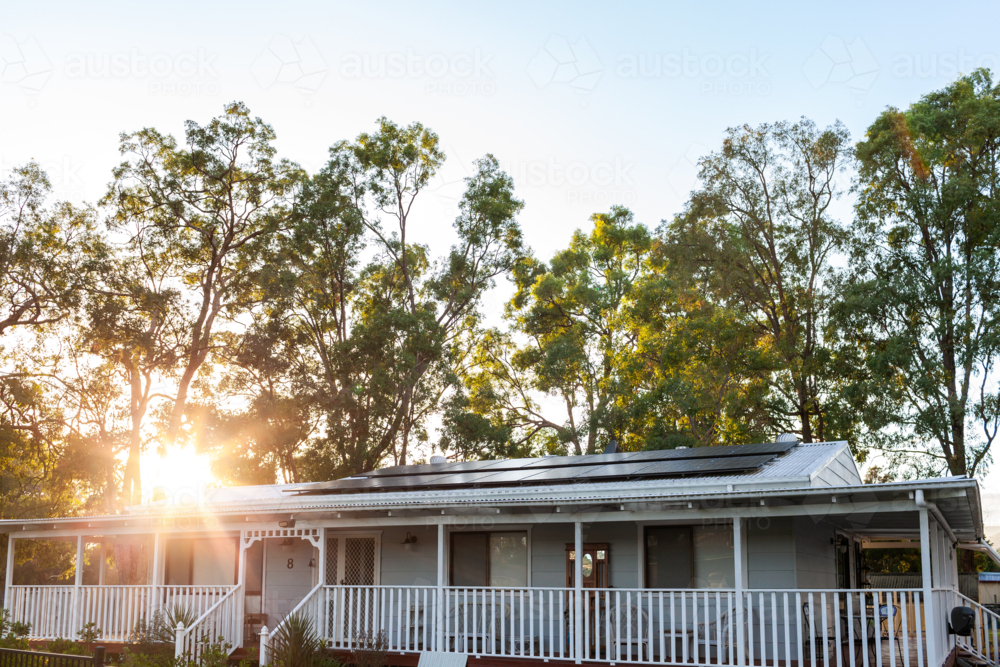 White country cottage with solar panels installed on tin roof with gum trees behind at sunrise - Australian Stock Image