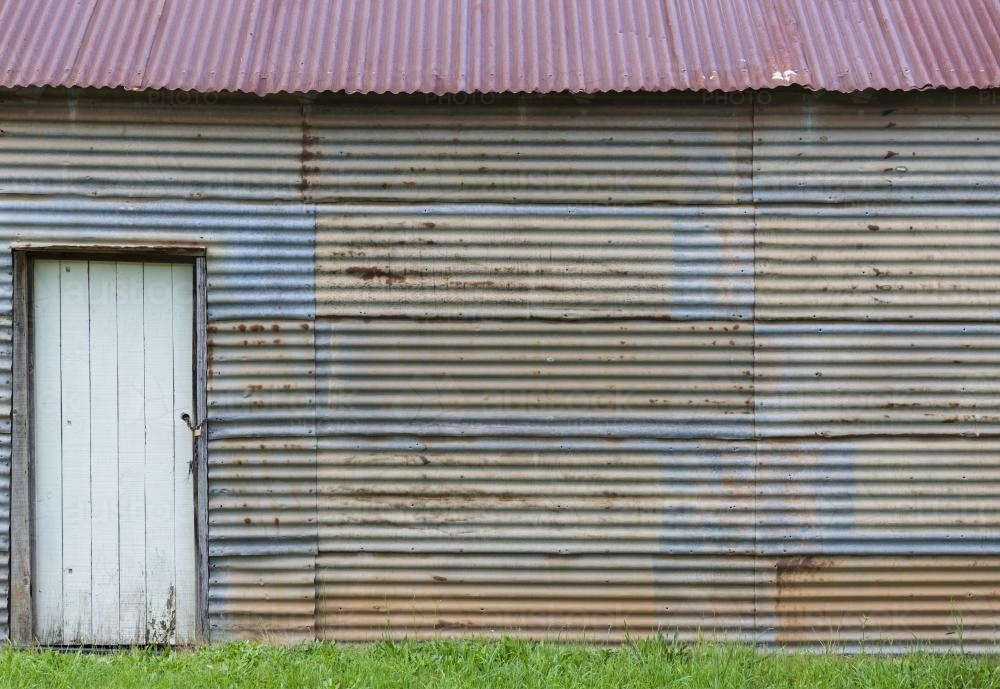 White door set in rusty wall of corrugated iron shed - Australian Stock Image