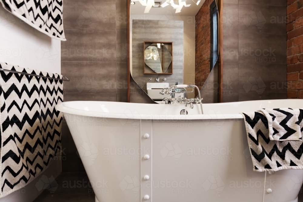 White free standing vintage style bath tub with chevron pattern black and white towels - Australian Stock Image