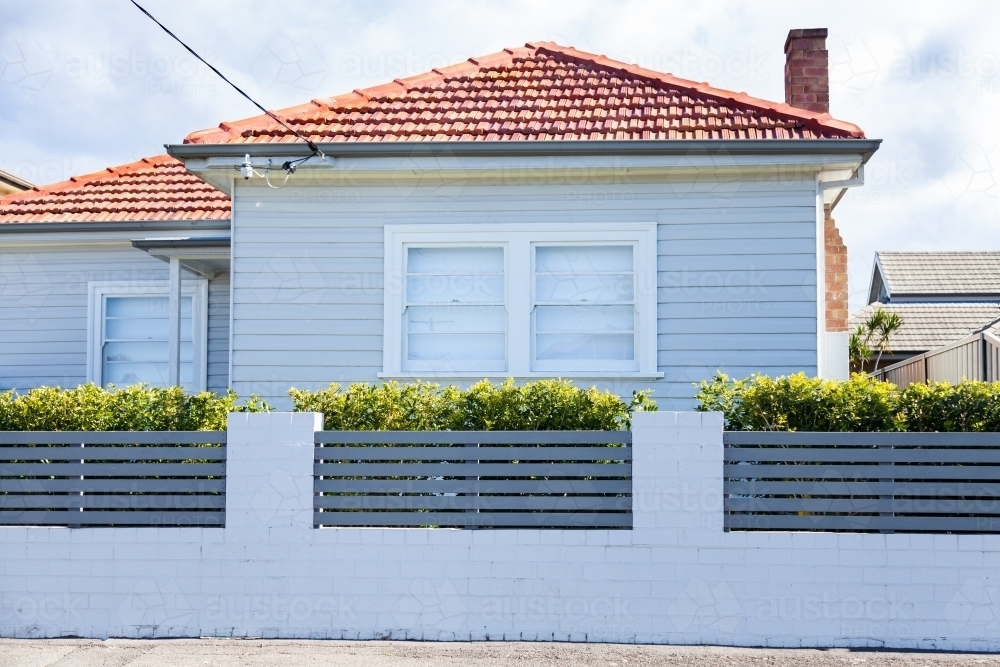 White house with red tiled roof on street, white brick fence - Australian Stock Image
