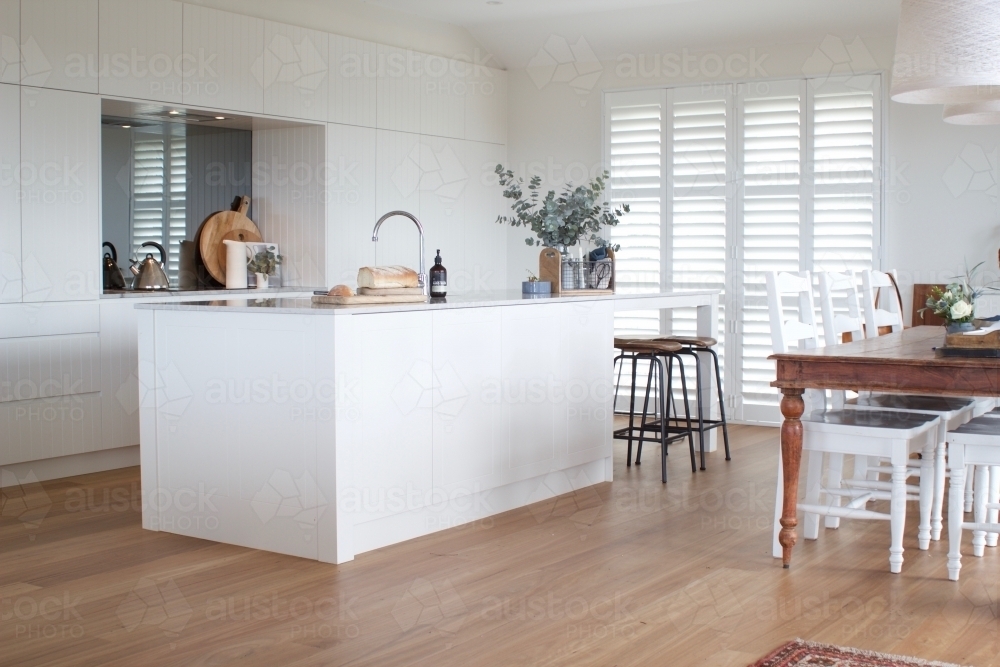 White kitchen with dining table, wooden floor and shutters - Australian Stock Image