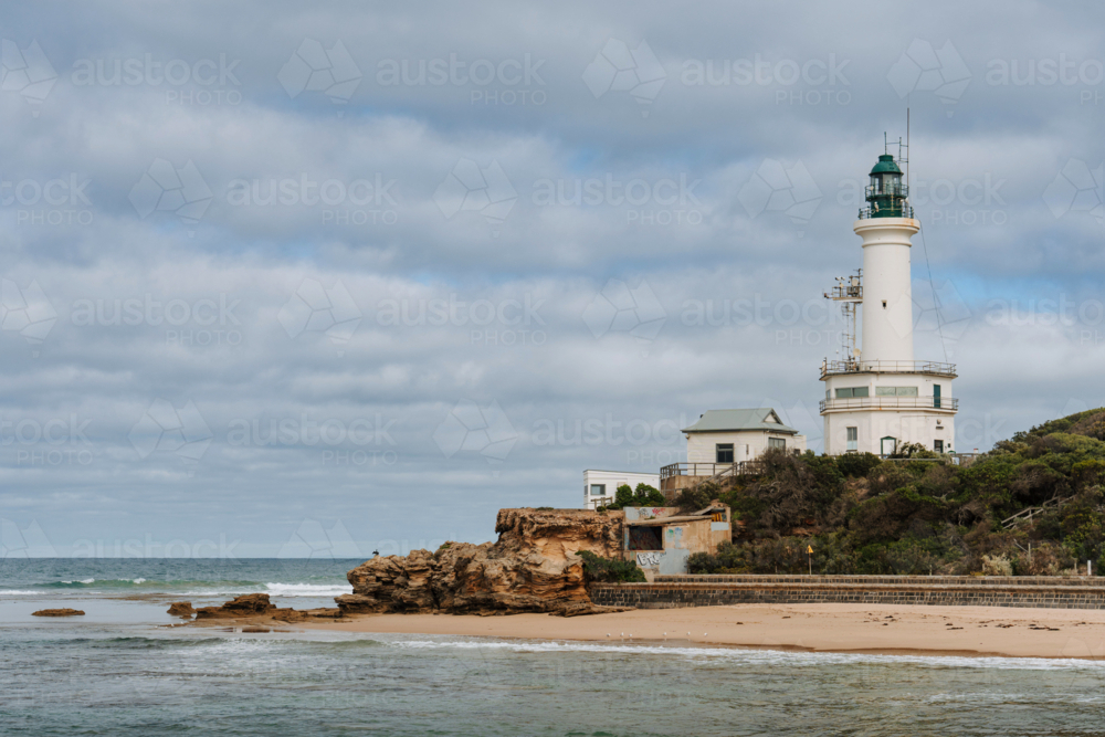 White lighthouse stands on a rocky headland overlooking the ocean - Australian Stock Image