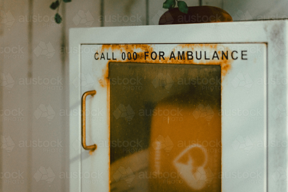 White metal cabinet mounted on a wall, labelled clearly with the text “CALL 000 FOR AMBULANCE” - Australian Stock Image