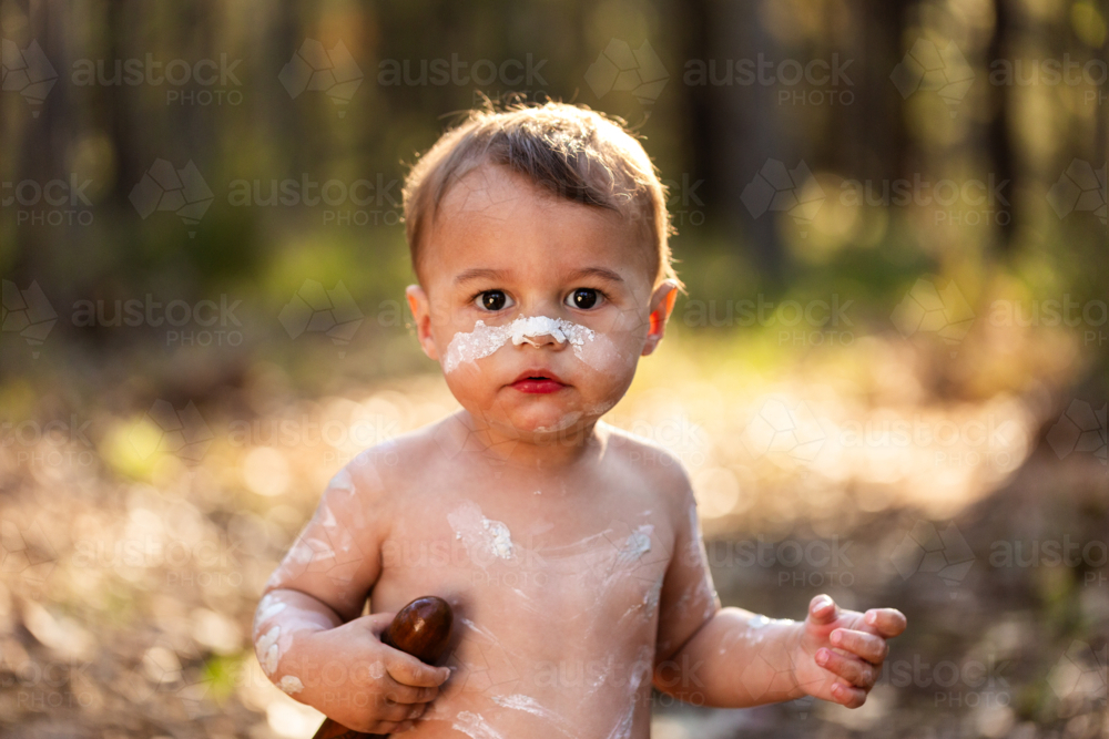 White ochre paint on Aboriginal child’s face in natural bushland with backlighting - Australian Stock Image