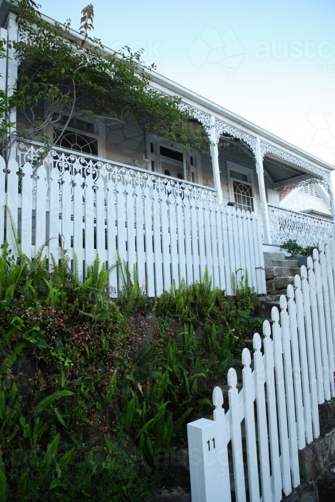 White picket fence in front of a house with a porch. - Australian Stock Image