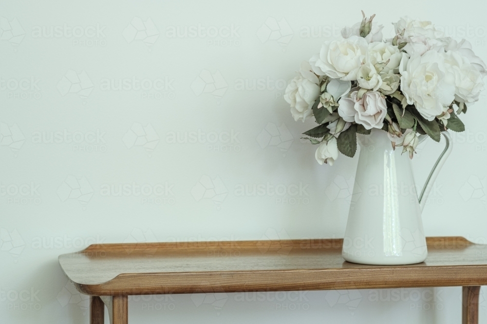 White Roses in a white vase on a timber hallway table inside a country home - Australian Stock Image