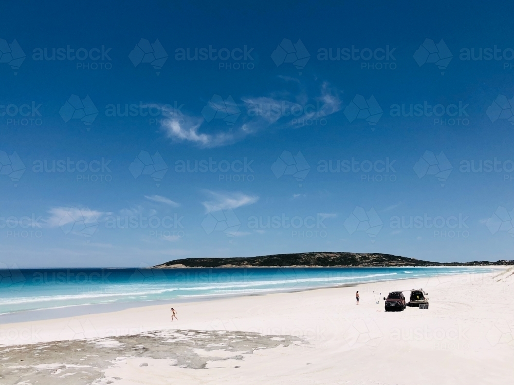 White sandy beach with blue oceans and two 4WDs stationary on sand with two figures - Australian Stock Image