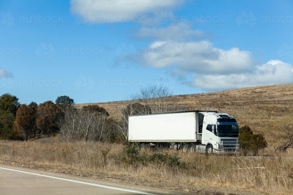 White truck on opposite side of divided highway transporting goods through rural Australia - Australian Stock Image