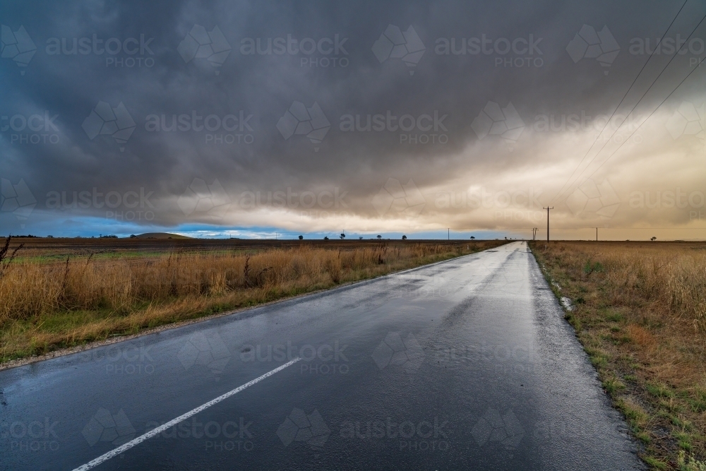 Wide angled view down a country road with bright gap under dark storm clouds - Australian Stock Image