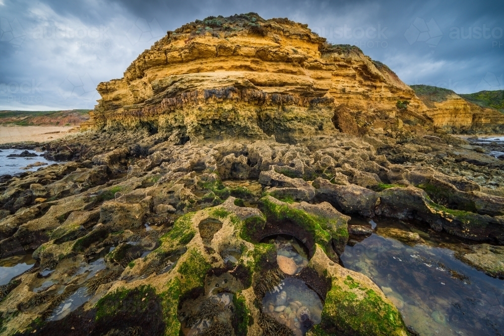 Wide angled view of rockpools below a rugged coastal headland under dramatic clouds - Australian Stock Image