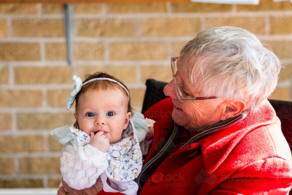 Wide blue eyed baby great grandchild held by great grandma - family generations - Australian Stock Image