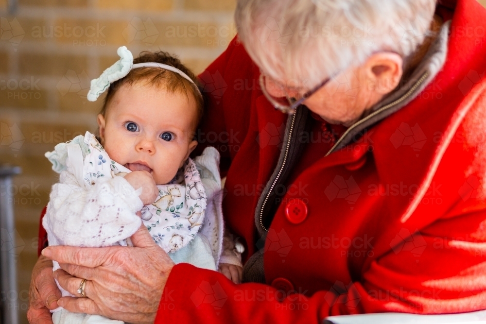 Wide blue eyed baby great grandchild held by great grandma - family generations - Australian Stock Image