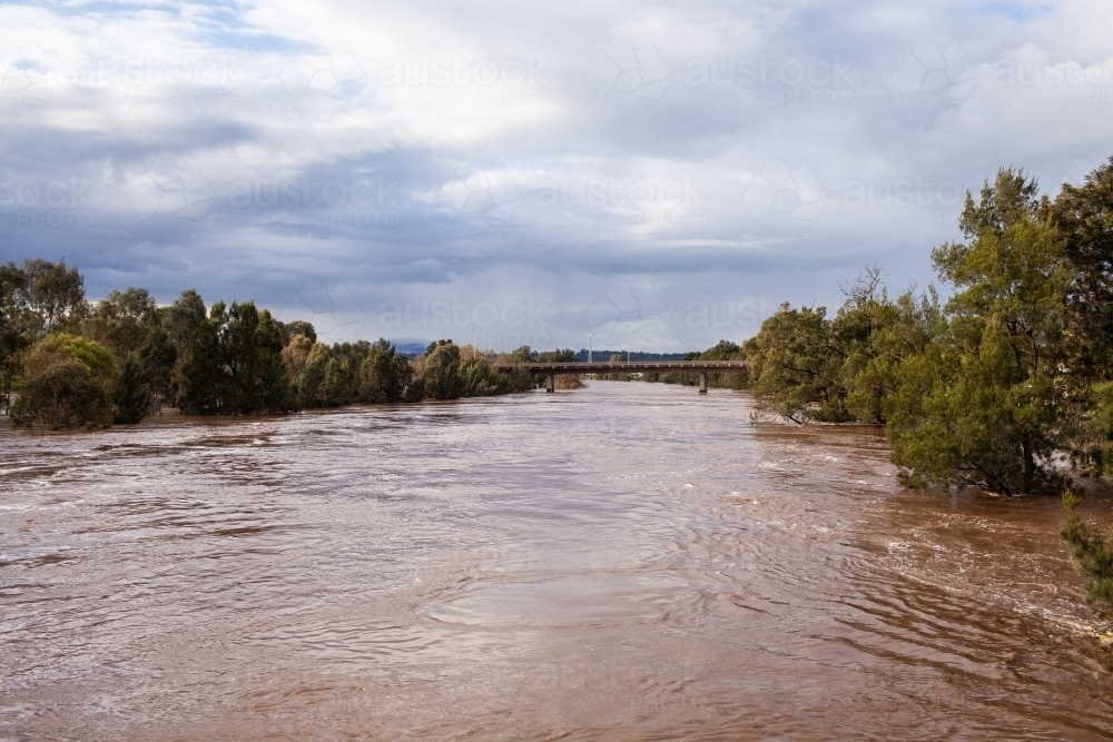 wide brown river full of floodwater during natural disaster flood - Australian Stock Image