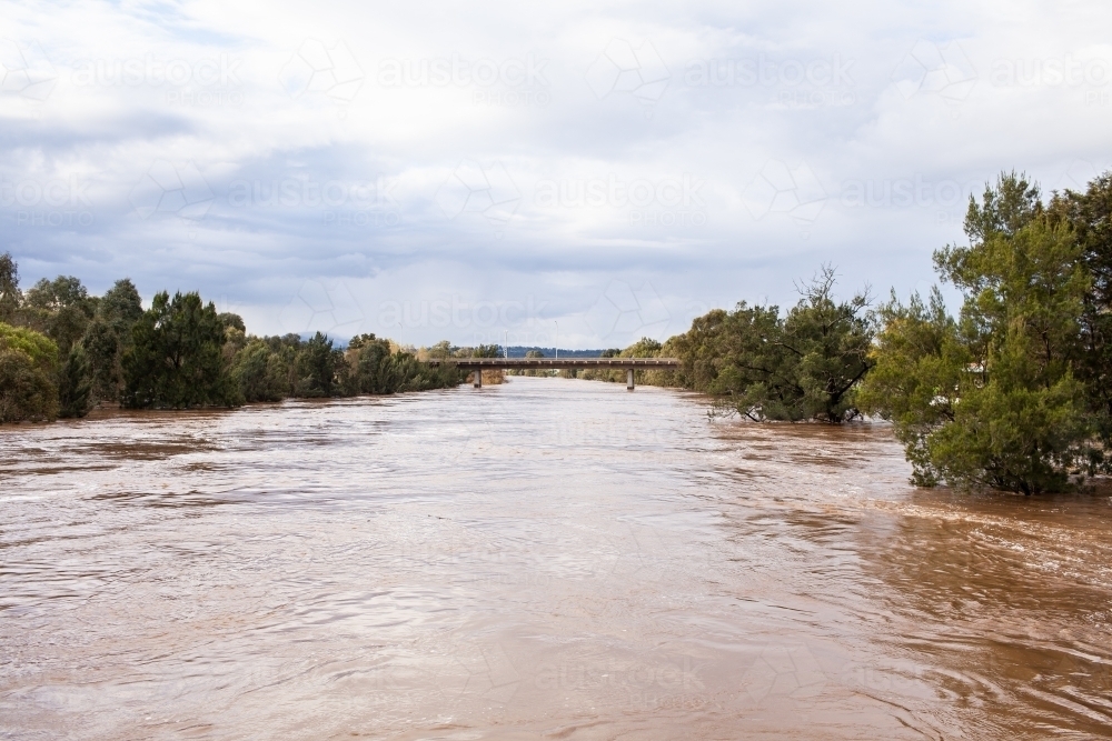 wide brown river full of floodwater during natural disaster flood - Australian Stock Image