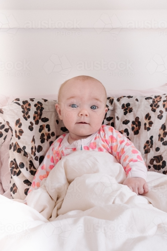 Wide eyed little baby girl in bed. - Australian Stock Image