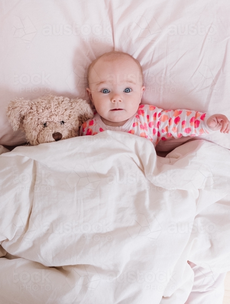 Wide eyed little girl in bed with teddy bear. - Australian Stock Image