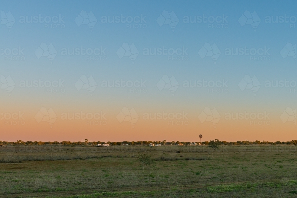 Wide paddock with caravans and a windmill in dusk light - Australian Stock Image