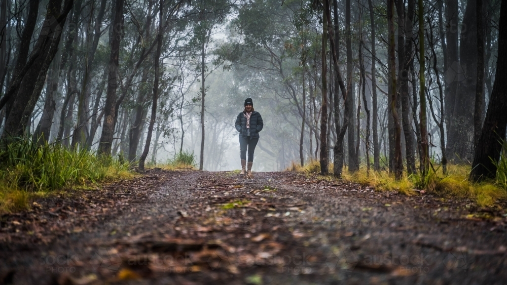 Wide shot of woman walking on foggy mountain track - Australian Stock Image