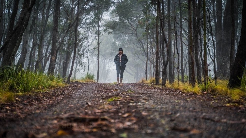 Wide shot of woman walking towards camera on foggy mountain track - Australian Stock Image