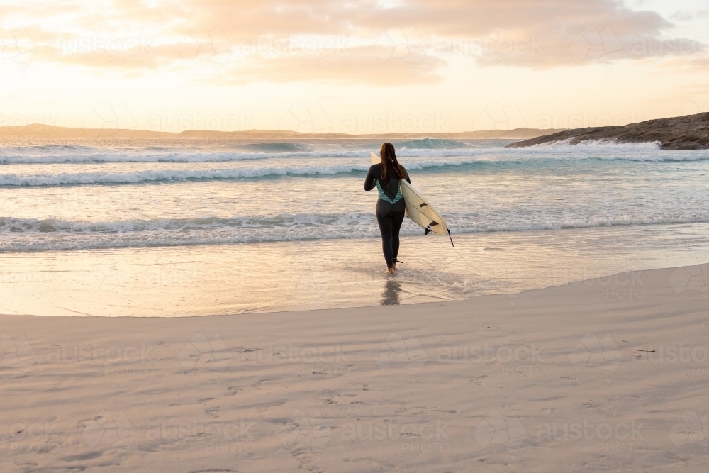 wide view of surfer heading into the surf at sunset - Australian Stock Image