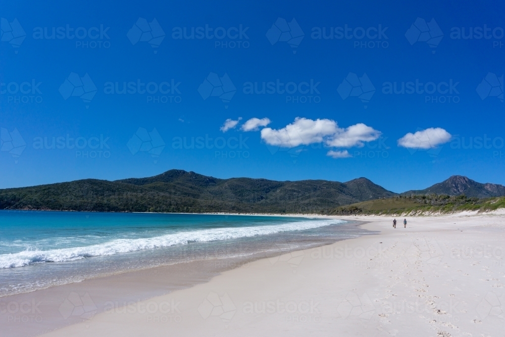 Wide, white sandy beach with a couple of people in the distance beneath a blue sky - Australian Stock Image