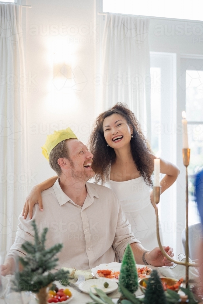 Wife and husband wearing Christmas crown at dining table - Australian Stock Image