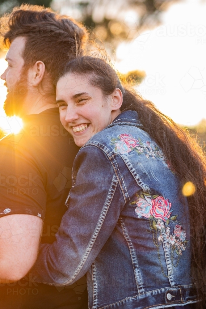 Wife hugging her husband from behind with golden sun flare - Australian Stock Image