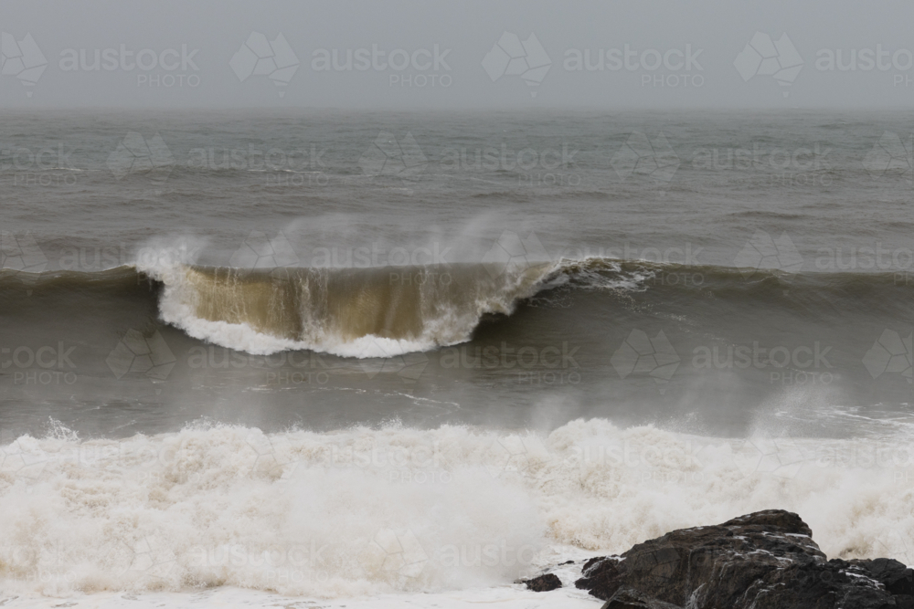 Wild weather with View of spray flying off wave breaking, white water in foreground and rocks - Australian Stock Image