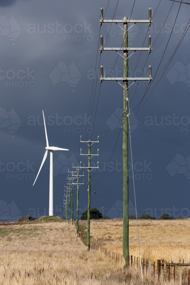 Image of Wind turbine alongside power lines and fence - Austockphoto