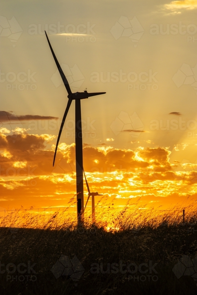Image of Wind turbine silhouette against sunset with rays - Austockphoto
