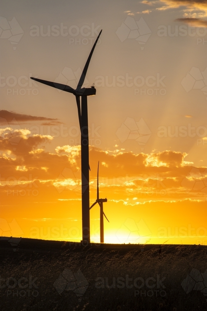 Wind turbine silhouette against sunset with rays - Australian Stock Image