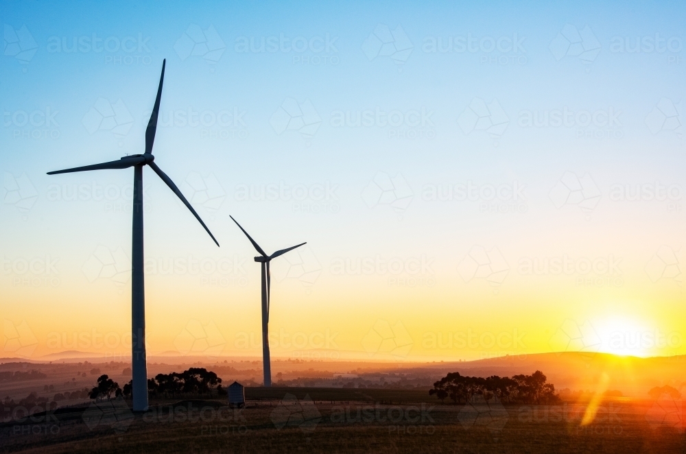 Wind turbine silhouettes with the sun rising over the horizon. - Australian Stock Image