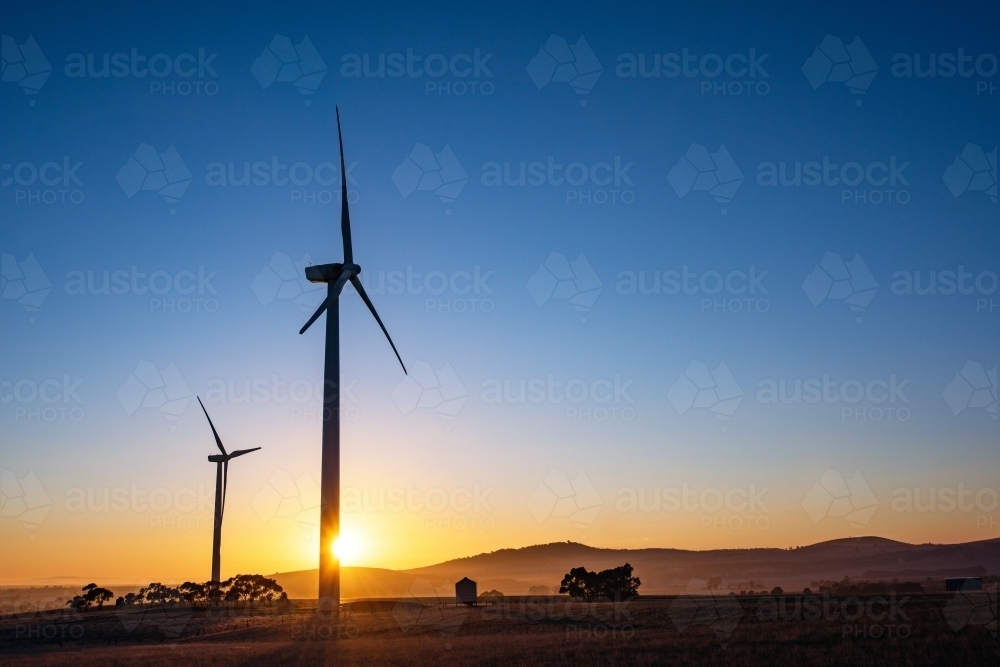 Wind turbine silhouettes with the sun shining through the turbine at sunrise - Australian Stock Image