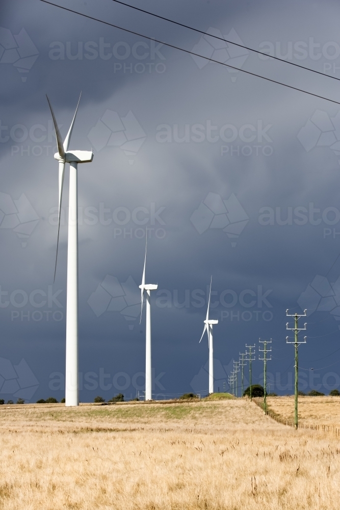 Wind turbines and power lines in paddock with incoming storm - Australian Stock Image