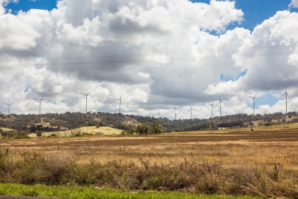 Wind turbines in distance on top of hill above paddock on farm - Australian Stock Image