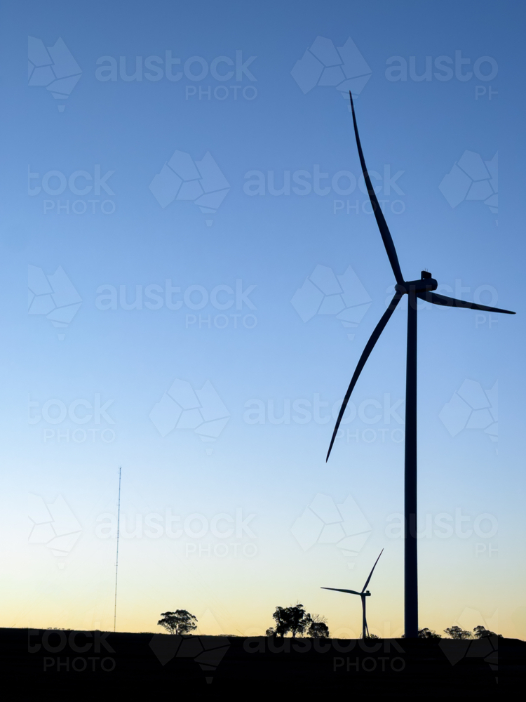 wind turbines in silhouette against fading blue sky at dusk - Australian Stock Image