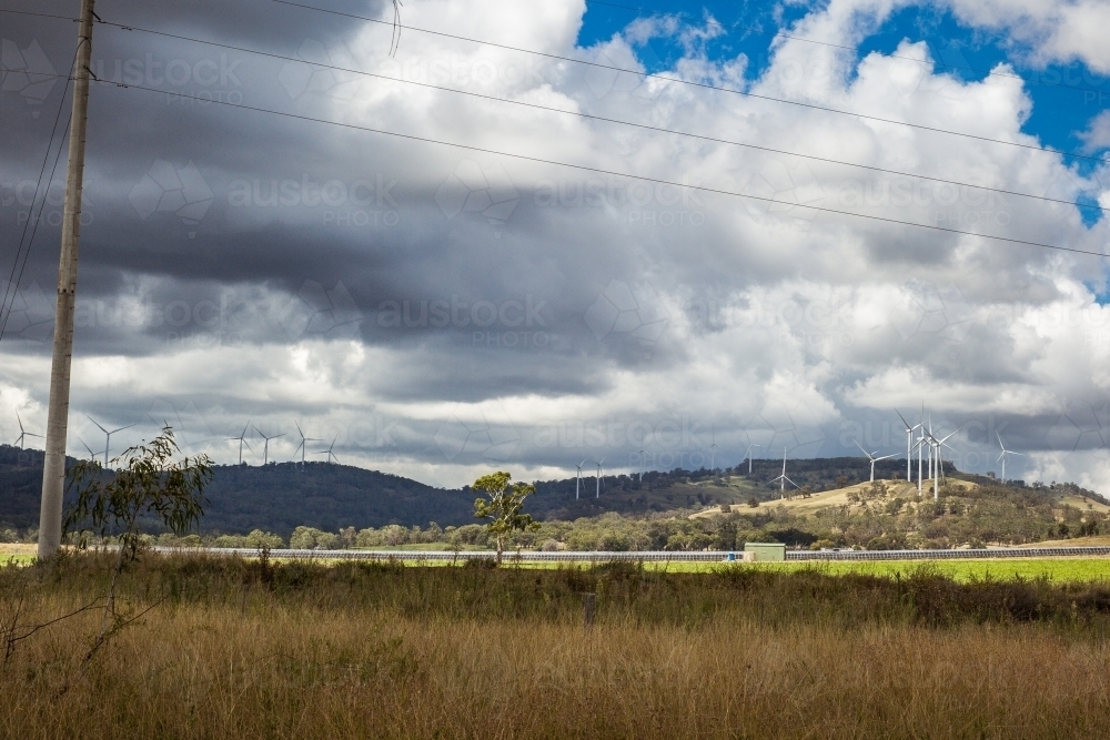 Wind turbines on hill above paddock with solar farm with cloudy sky and power lines - Australian Stock Image