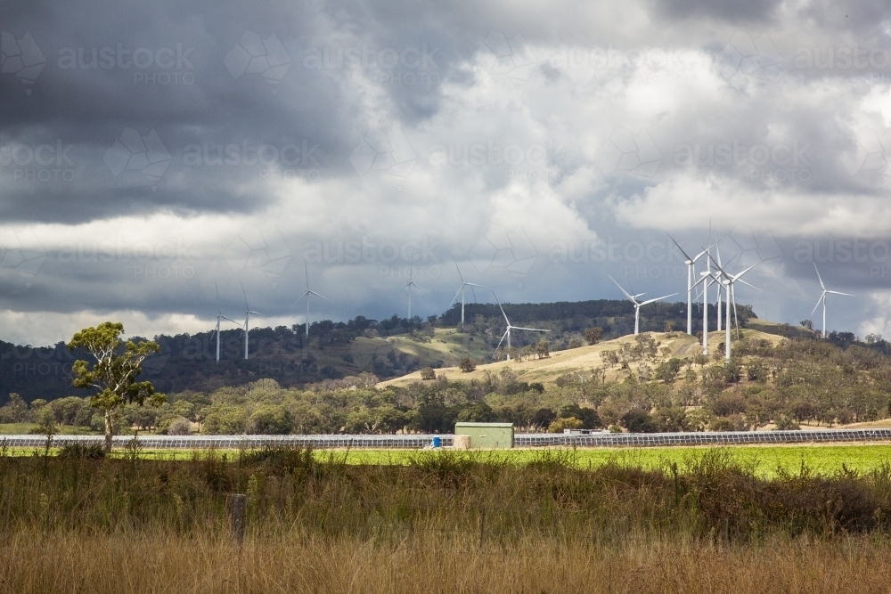 Wind turbines on hill above solar farm in paddock on farm - Australian Stock Image
