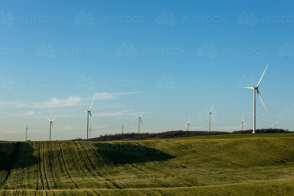 wind turbines on hill tops with farmland in foreground - Australian Stock Image