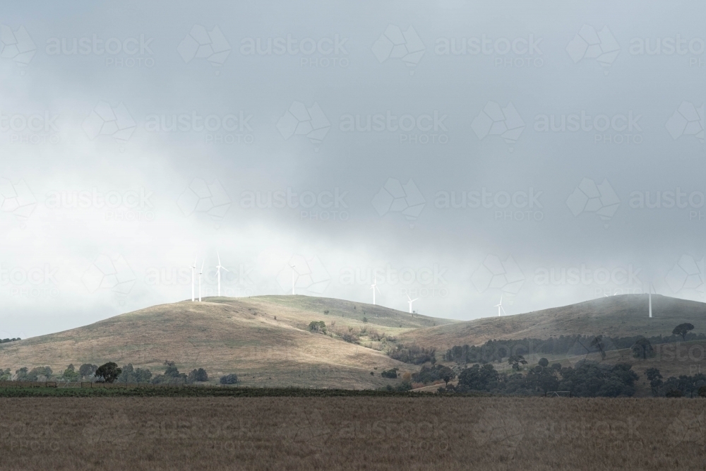 wind turbines on the hilly horizon with low lying cloud - Australian Stock Image