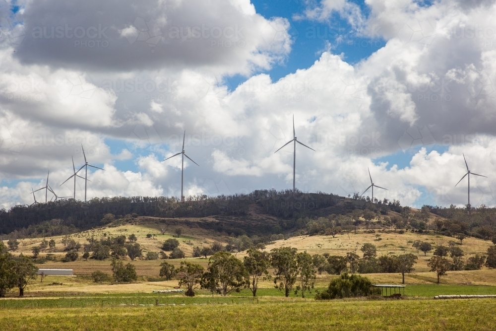 Wind turbines on top of hill above paddocks on farm with cloudy sky - Australian Stock Image