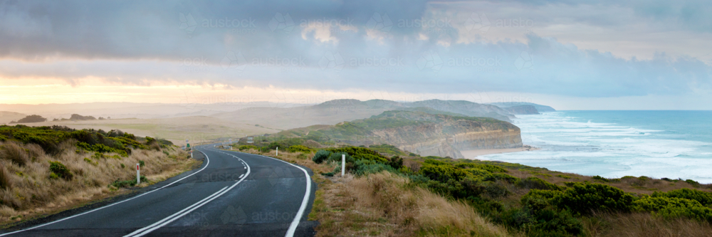 Winding coastal road overlooking cliffs and ocean under a dramatic morning sky. - Australian Stock Image