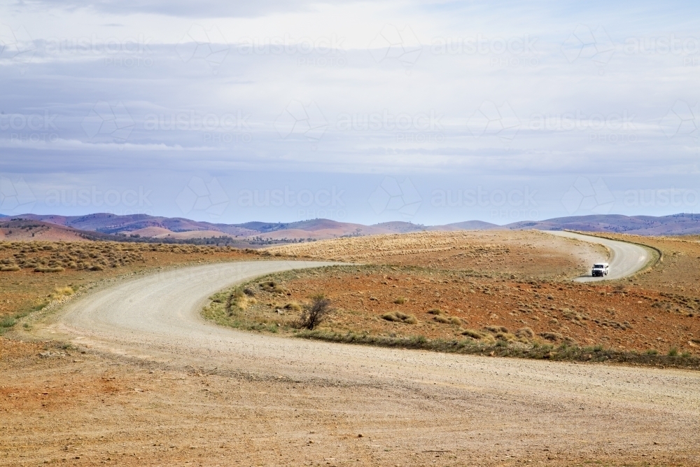 Winding dirt road with vehicle approaching - Australian Stock Image