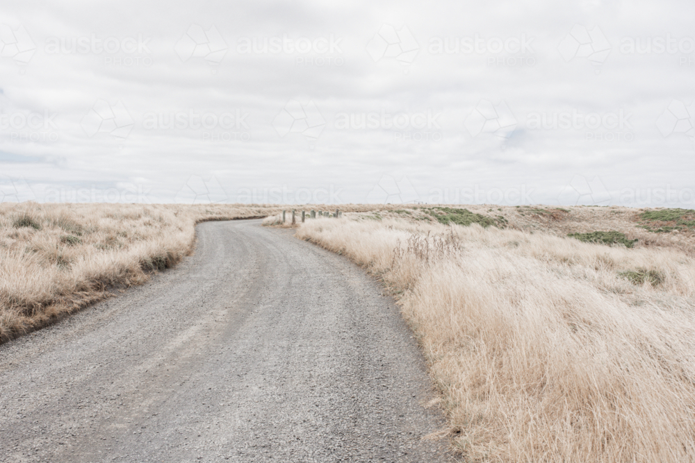 Winding, unsealed, gravel track through dry grasses - Australian Stock Image