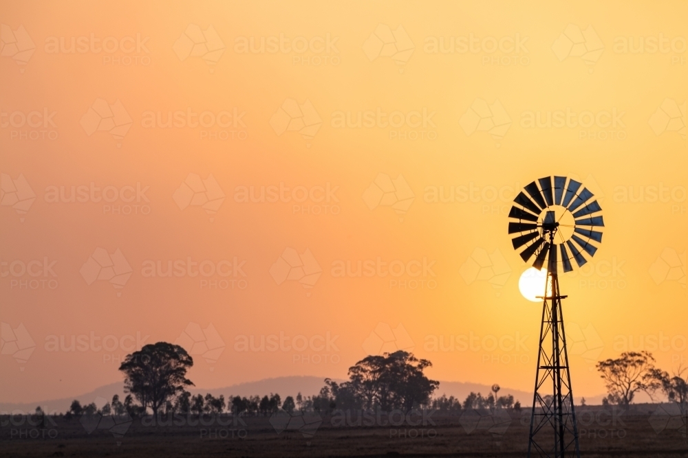 Windmill against a smoky sunset in drought conditions - Australian Stock Image