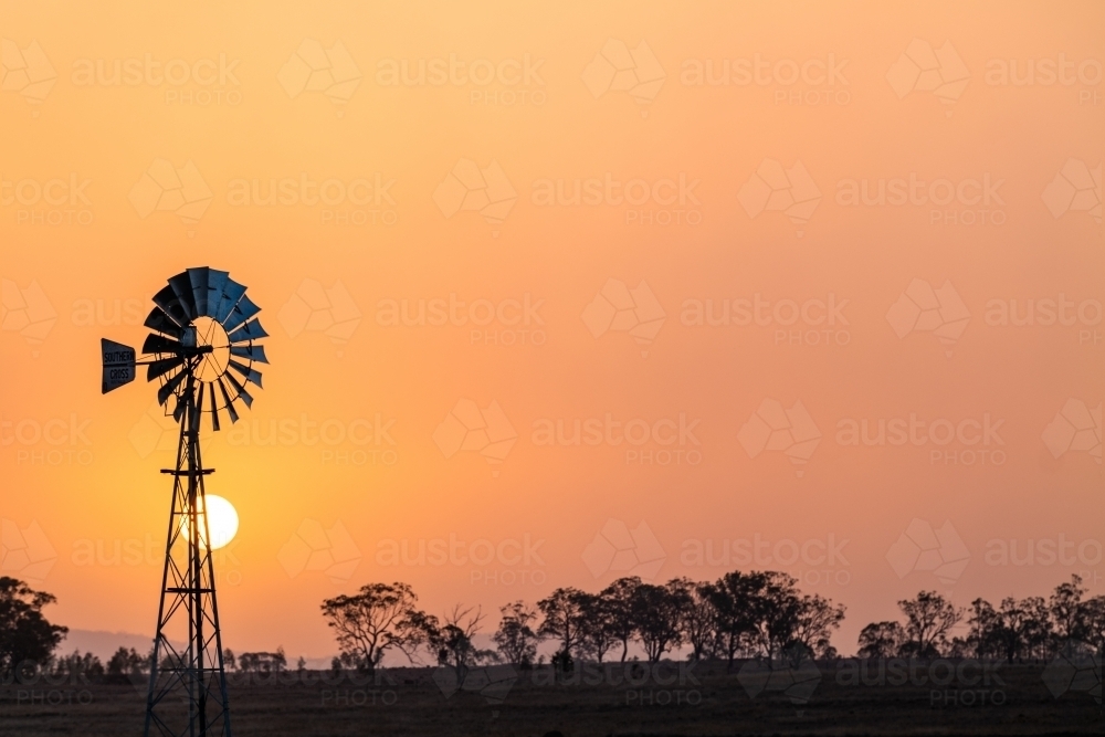 Windmill against a smoky sunset in drought conditions - Australian Stock Image