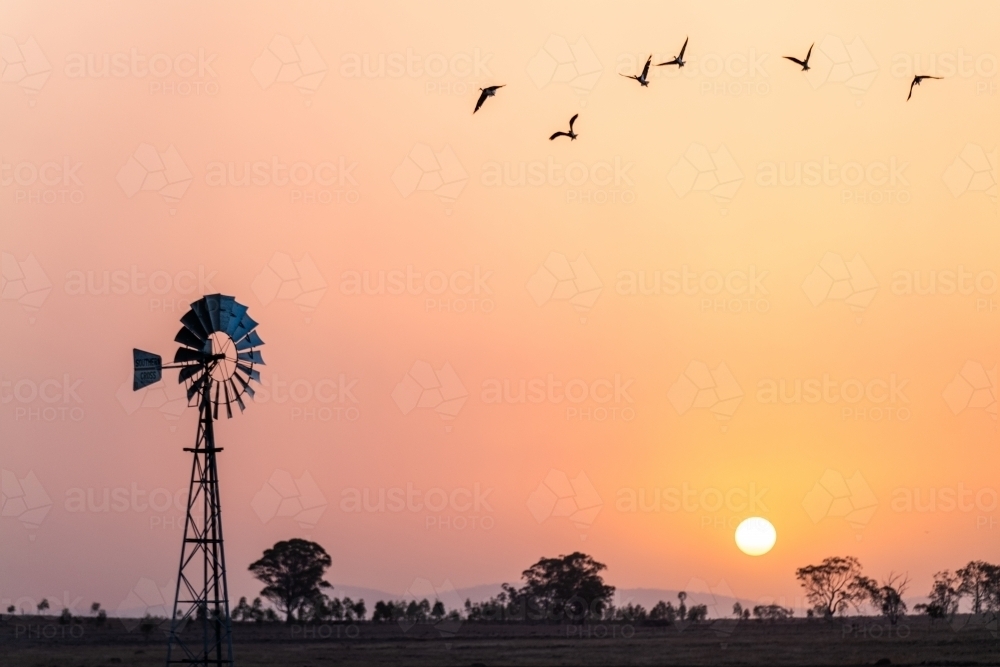 Windmill against a smoky sunset in drought conditions - Australian Stock Image